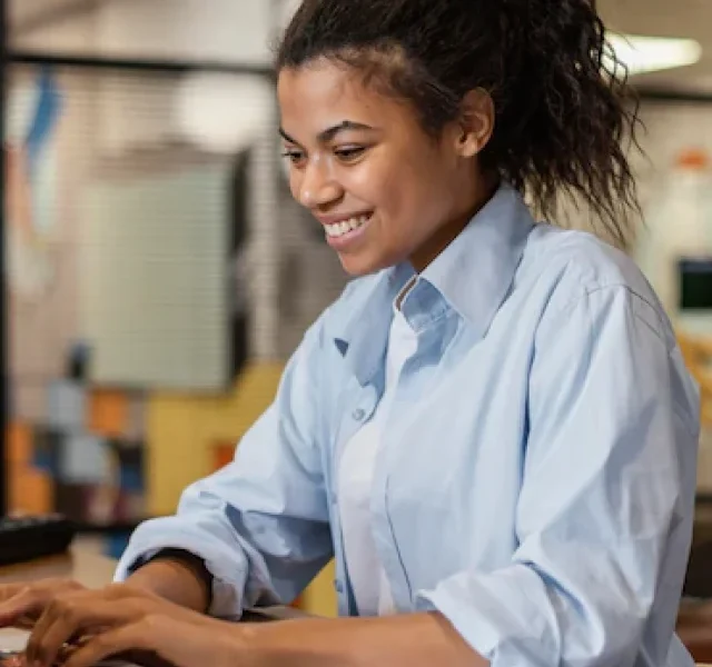 vista-lateral-de-uma-mulher-sorridente-trabalhando-com-um-laptop-no-escritorio_23-2148908808